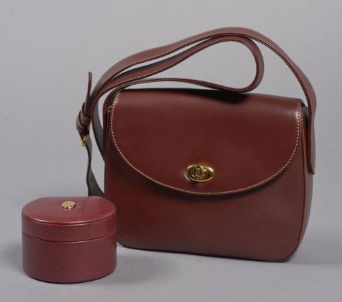 MUST DE CARTIER, Sac porté épaule en cuir bordeaux avec bandoulière réglable et garniture en métal doré, une poche à l'arrière, intérieur en toile bordeaux, une poche zippée. Carte d'authentification. Dimensions: 17.5 x 21 cm. Petits manques sur le cuir, 