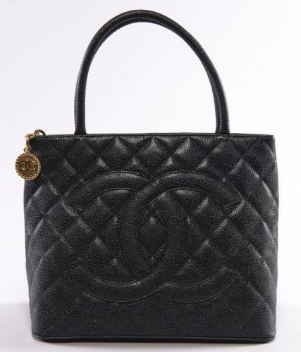 CHANEL, Médaillon en cuir grainé noir, deux anses portées main, une poche au dos, fermeture par zip retenant une pendeloque en métal doré siglé, intérieur en cuir noir à deux poches dont une zippée. Carte d'authenticité. 24 x 34 cm. Très bel état.