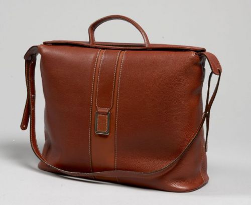 COURREGES, Sac d'épaule en cuir cognac souple parcouru d'une bande en cuir tabac. Une anse bandoulière réglable, une poignée sous rabat. Plaque en métal argenté recouverte de cuir monogrammé. Deux grandes poches plaquées à l'arrière. Double rabat magnétiq
