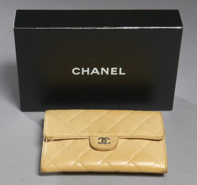 CHANEL Porte-monnaie matelassé en cuir beige avec sigle argent sur le rabat. 3 compartiments avec porte-monnaie et porte-cartes. Usures. Bon état