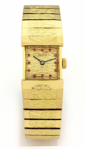 PATEK PHILIPPE REF. 3409 YELLOW GOLD.Patek Philippe, movement No. 977818, case No. 2622853.Ref. 3409. Made in 1961..Fine, unusual and rare, rectangular, curved, 18K yellow gold.wristwatch with ruby-set gold dial and an integral hammered and.polished 18K y