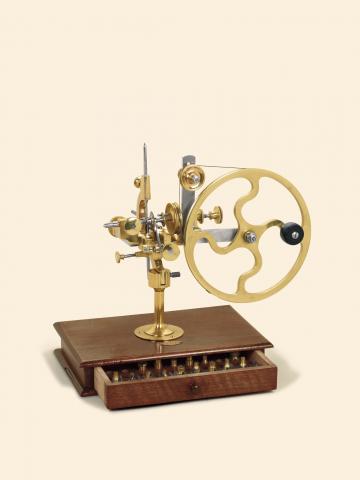 Sandoz Fils Co., La Chaux-de-Fonds Bienne, circa 1890. Fine brass and steel rounding up tool. Large crank lever wheel, horizontal depth slide controlled by a knurled nut, two stop posts, wooden base with a drawer for additional cutters and cutter chuc