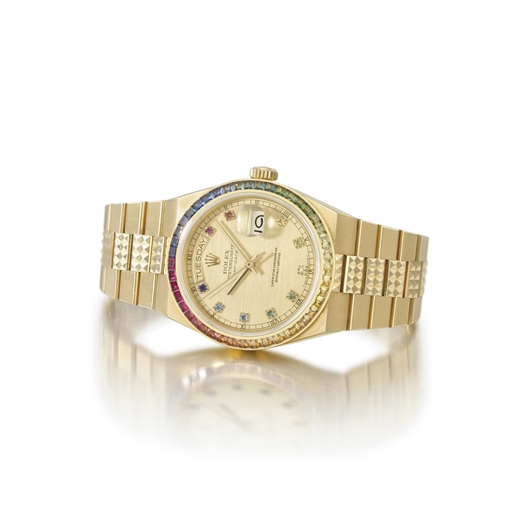 Rolex. An unusual 18K gold tonneau-shaped wristwatch with day, date, sweep centre seconds, bracelet, rainbow-coloured multi-gem set numerals and bezel